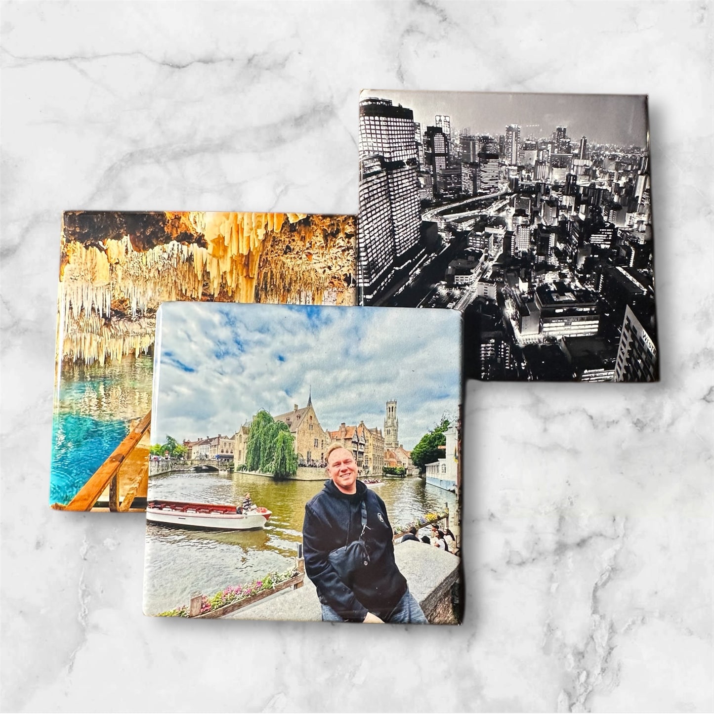 Three photo magnets of different scenes of travel on a white marble background.