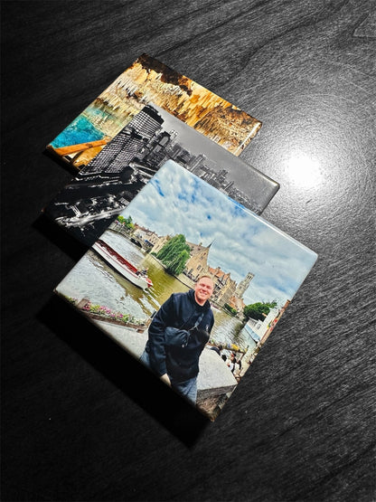 Three square photo magnets with printed scenic and portrait images, arranged diagonally on a dark wood surface.